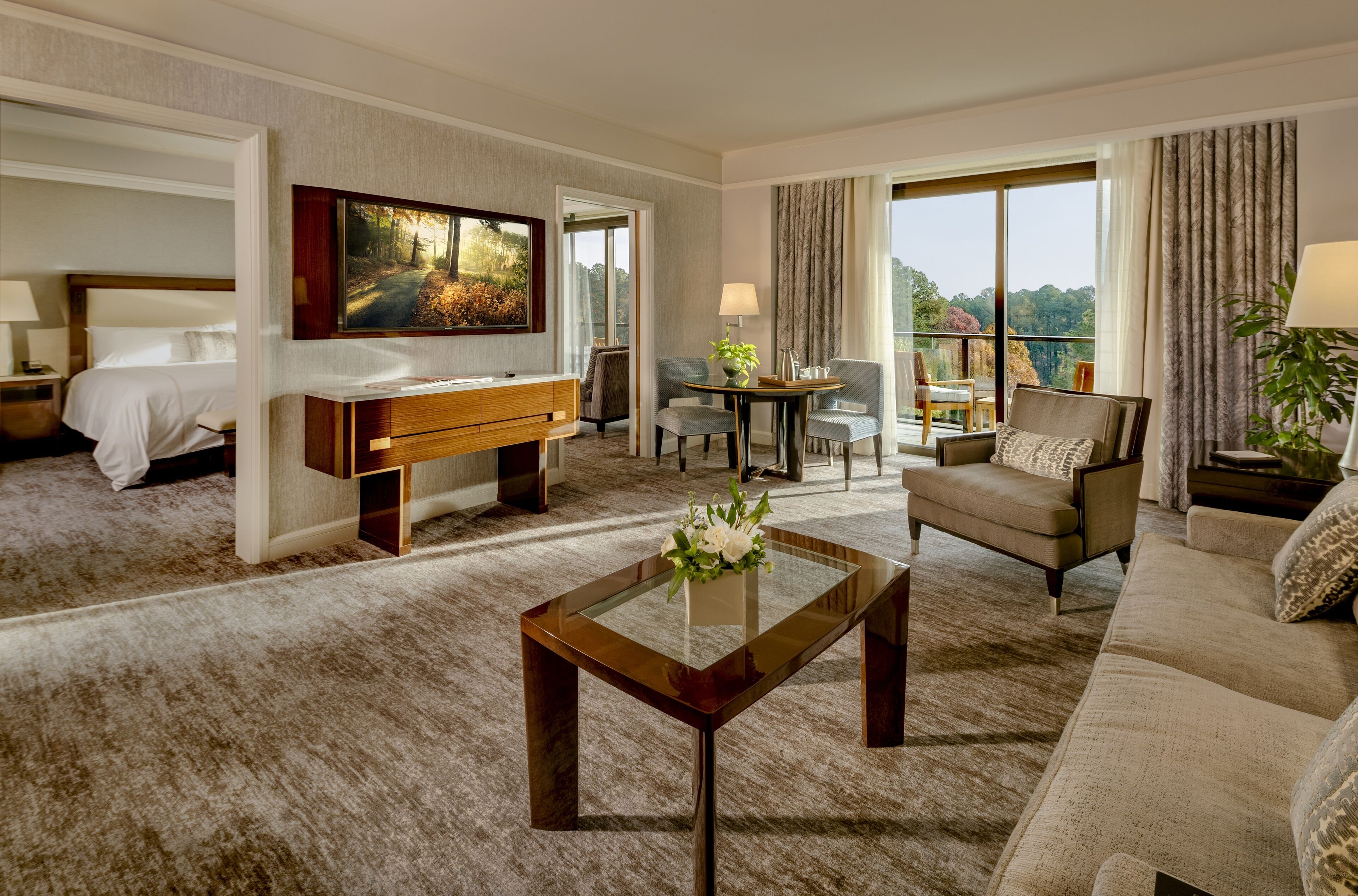 A hotel room with a bed, a sitting area with a sofa and chairs, a coffee table with flowers, and a large window offering a view.