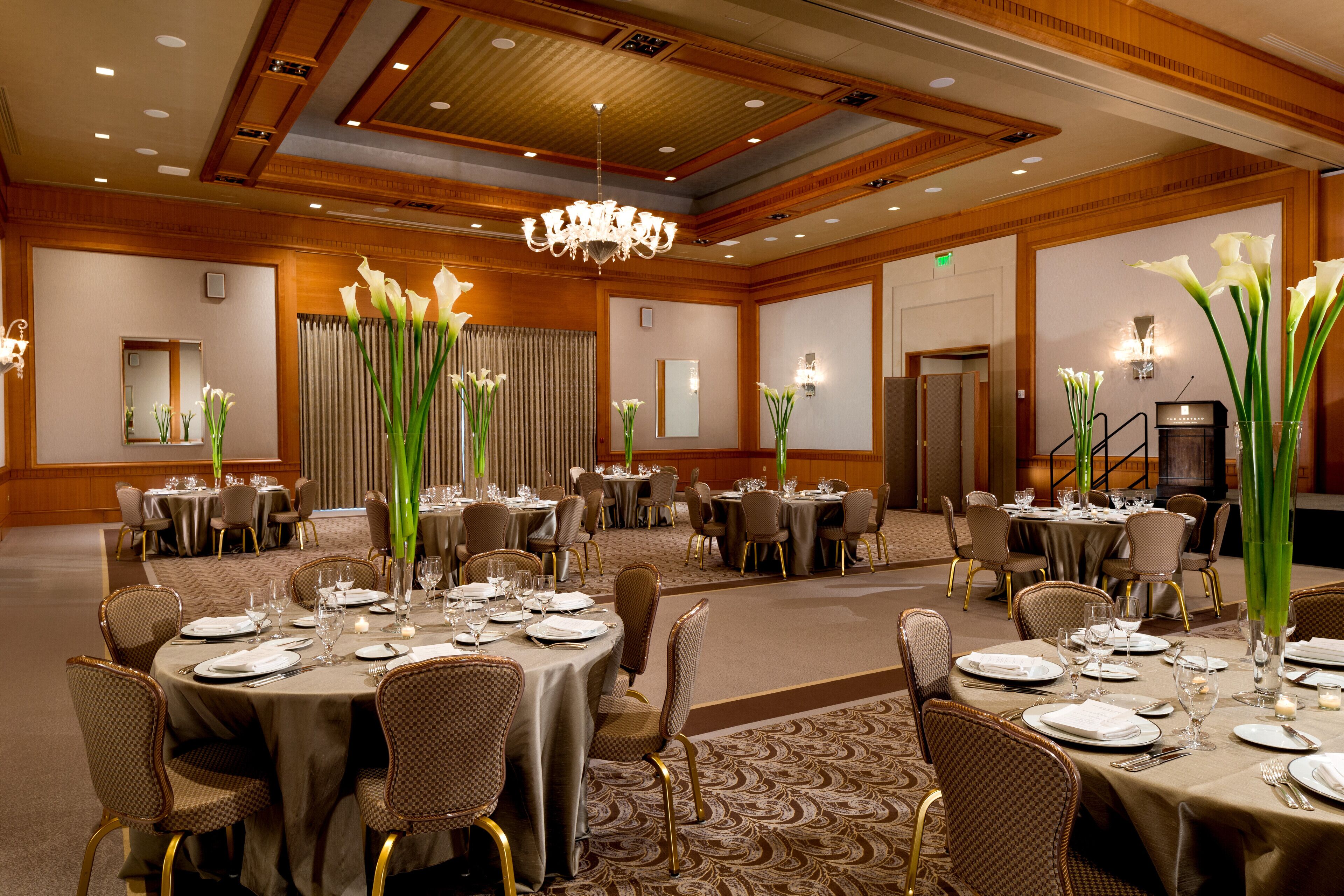 Une salle de banquet avec des tables rondes dressées pour le repas, équipées de chaises et de couverts.
