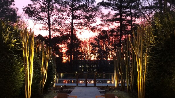 An outdoor seating area with a view of a sunset over a forested area. - The Umstead Hotel and Spa (Cary)