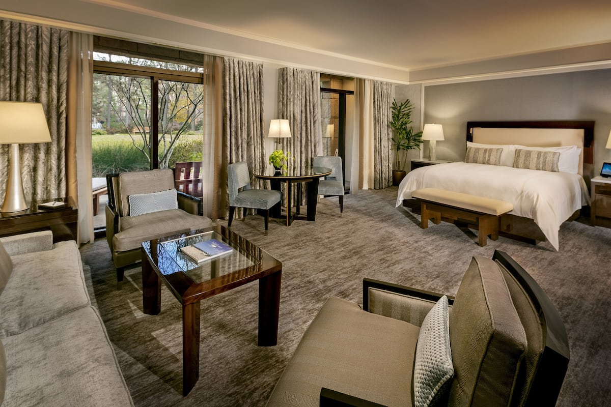 A hotel room with a large bed, a sofa, a coffee table, and a desk with a lamp.