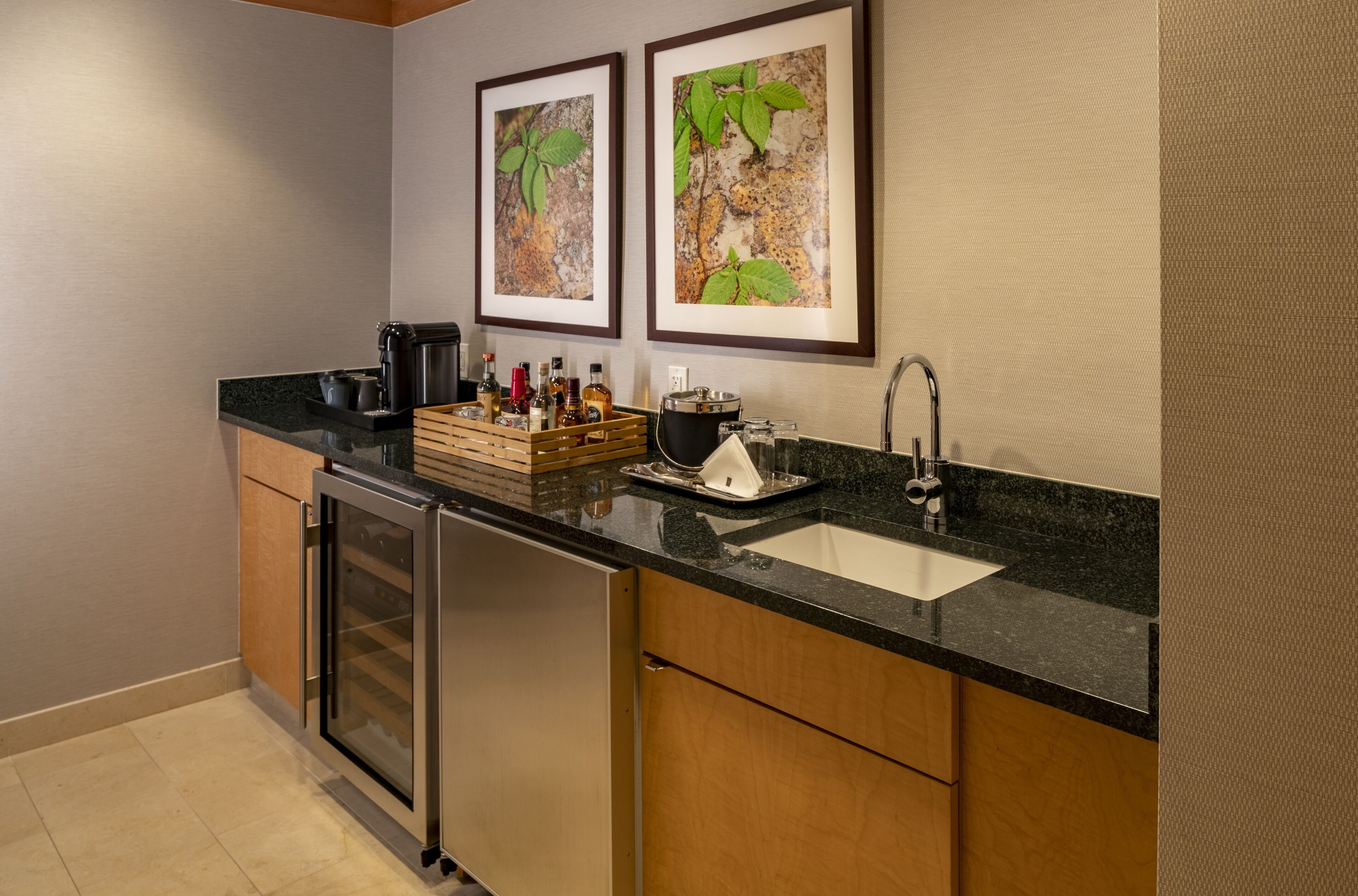 A modern kitchen with a built-in dishwasher, a sink, and a coffee machine. There are framed pictures on the wall and a wooden crate with bottles on the counter.