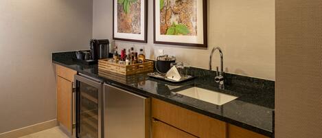 A modern kitchen with a built-in dishwasher, a sink, and a coffee machine. There are framed pictures on the wall and a wooden crate with bottles on the counter.