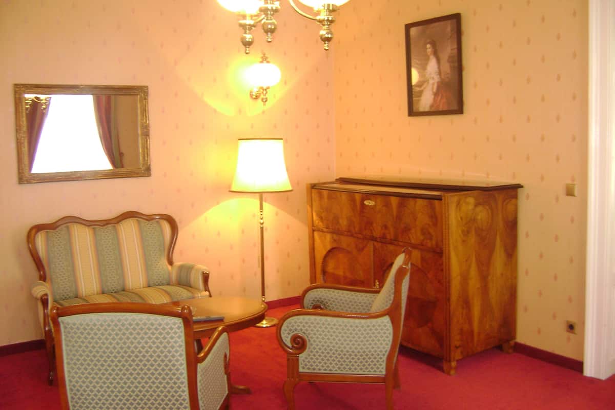 A room with a wooden cabinet, two upholstered chairs, a small table, a floor lamp, and a mirror on the wall.