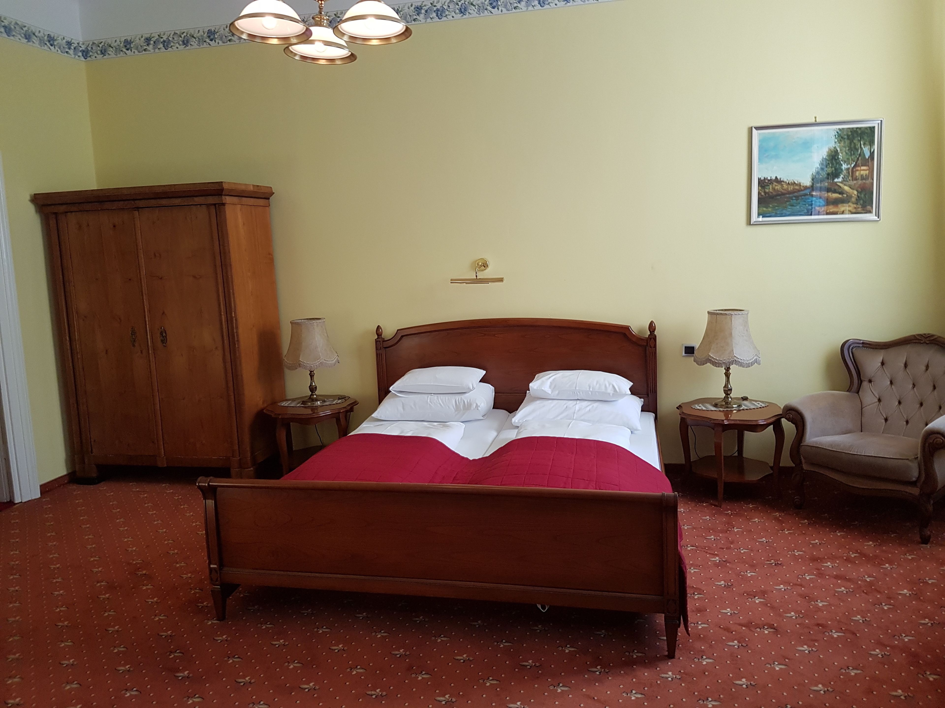 A bedroom with a wooden bed, two bedside tables with lamps, a chair, a wardrobe, and a painting on the wall.