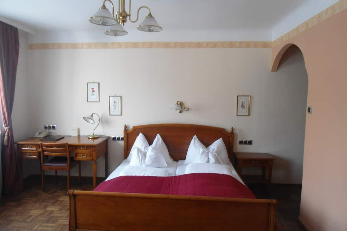 A hotel room with a wooden bed, a desk with a telephone, a lamp, and framed pictures on the wall.