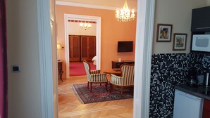 Une chambre d’hôtel avec un parquet en bois dispos é en chevrons, un coin repas avec des chaises à rayures, un lustre, une télévision et une kitchenette équipée d’un four à micro-ondes.
