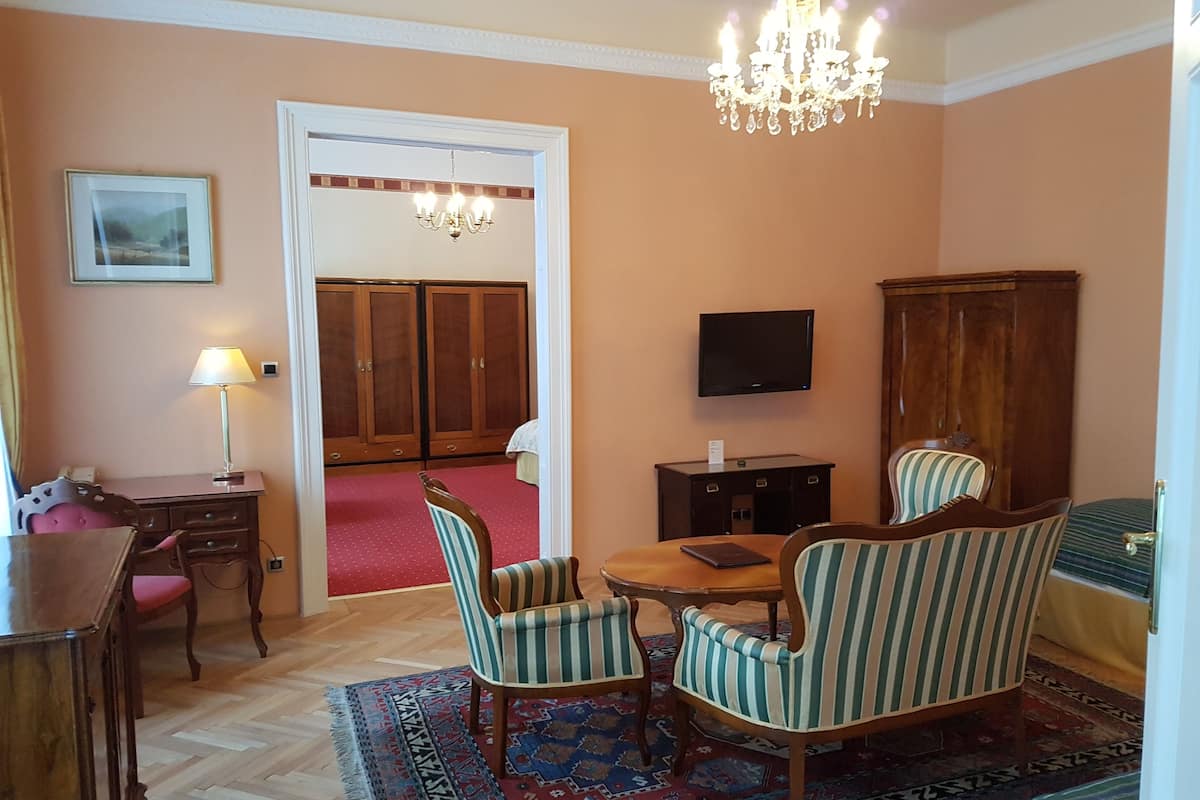 A room with a wooden desk, two striped armchairs, a chandelier, a television, and a wardrobe.