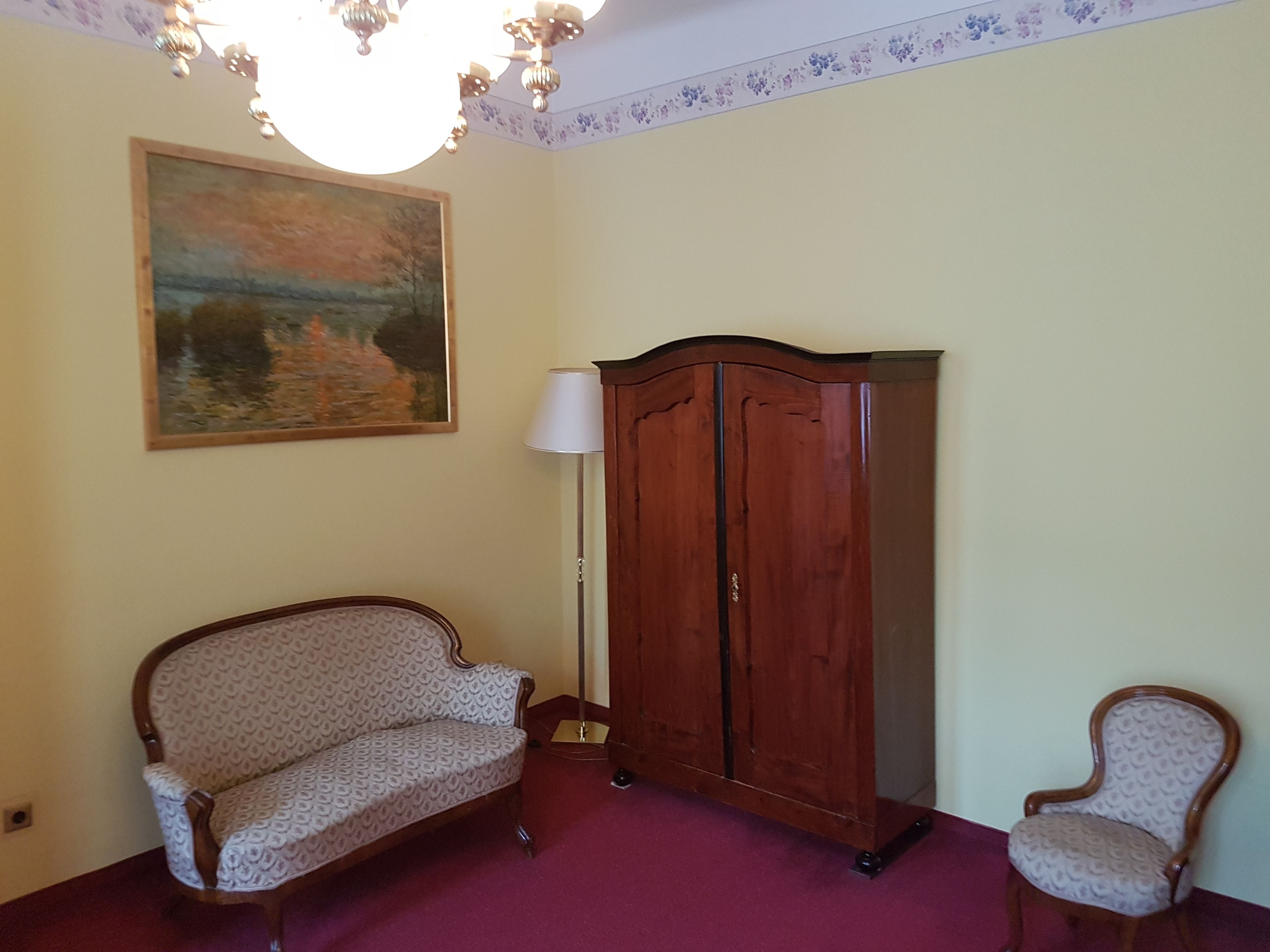 Une pièce avec un canapé à motifs, une armoire en bois, un lampadaire et un tableau accroché au mur.