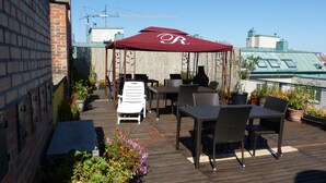 Une terrasse sur le toit, aménagée avec du mobilier d’extérieur, un espace salon couvert et des plantes en pot.