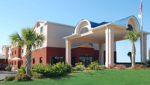 A hotel with a modern architectural design, featuring a covered entrance area, palm trees, and a flagpole. - Comfort Inn & Suites Chipley (Chipley)