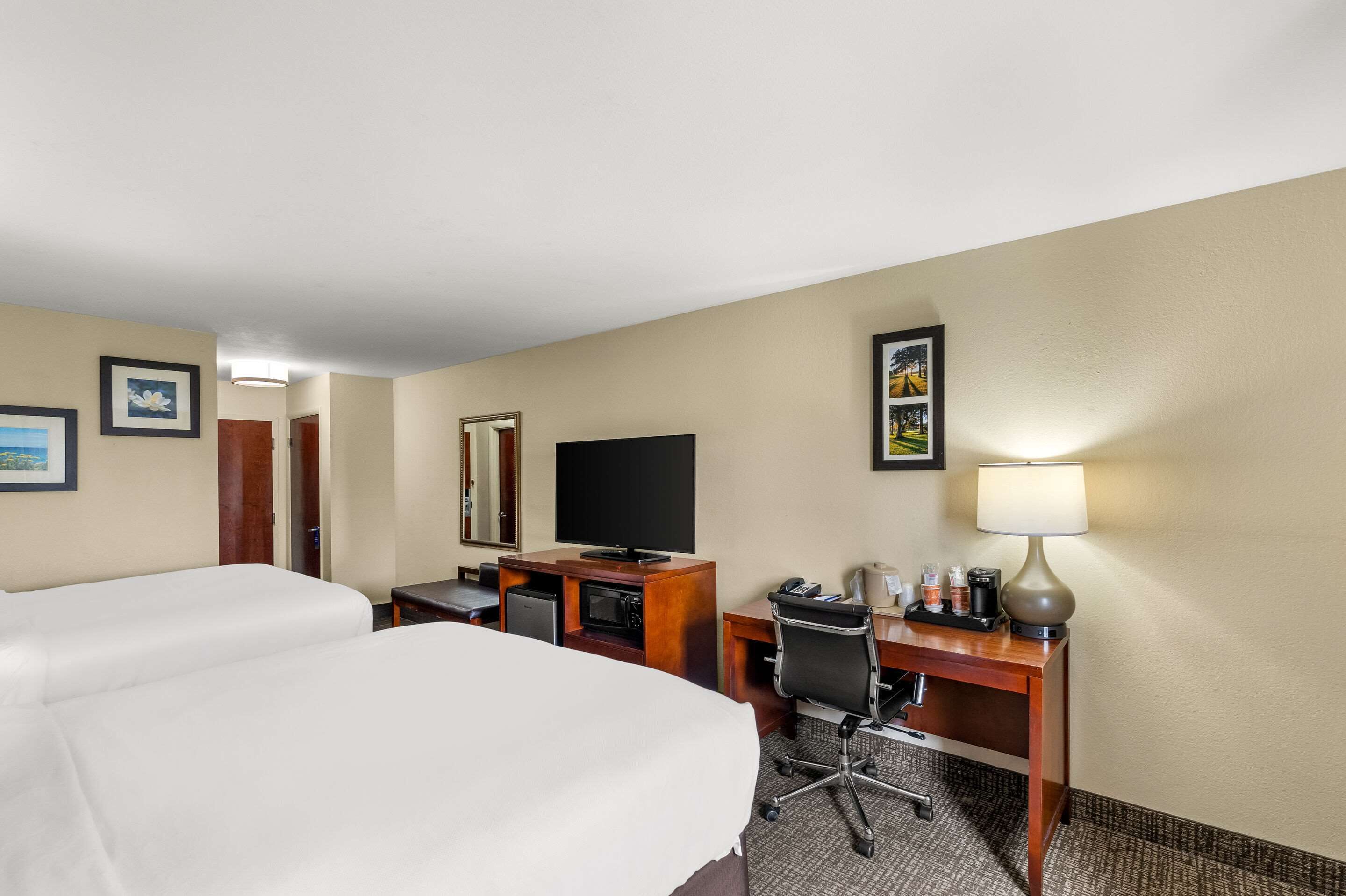 A hotel room with two beds, a desk with a computer, a television, and a lamp.