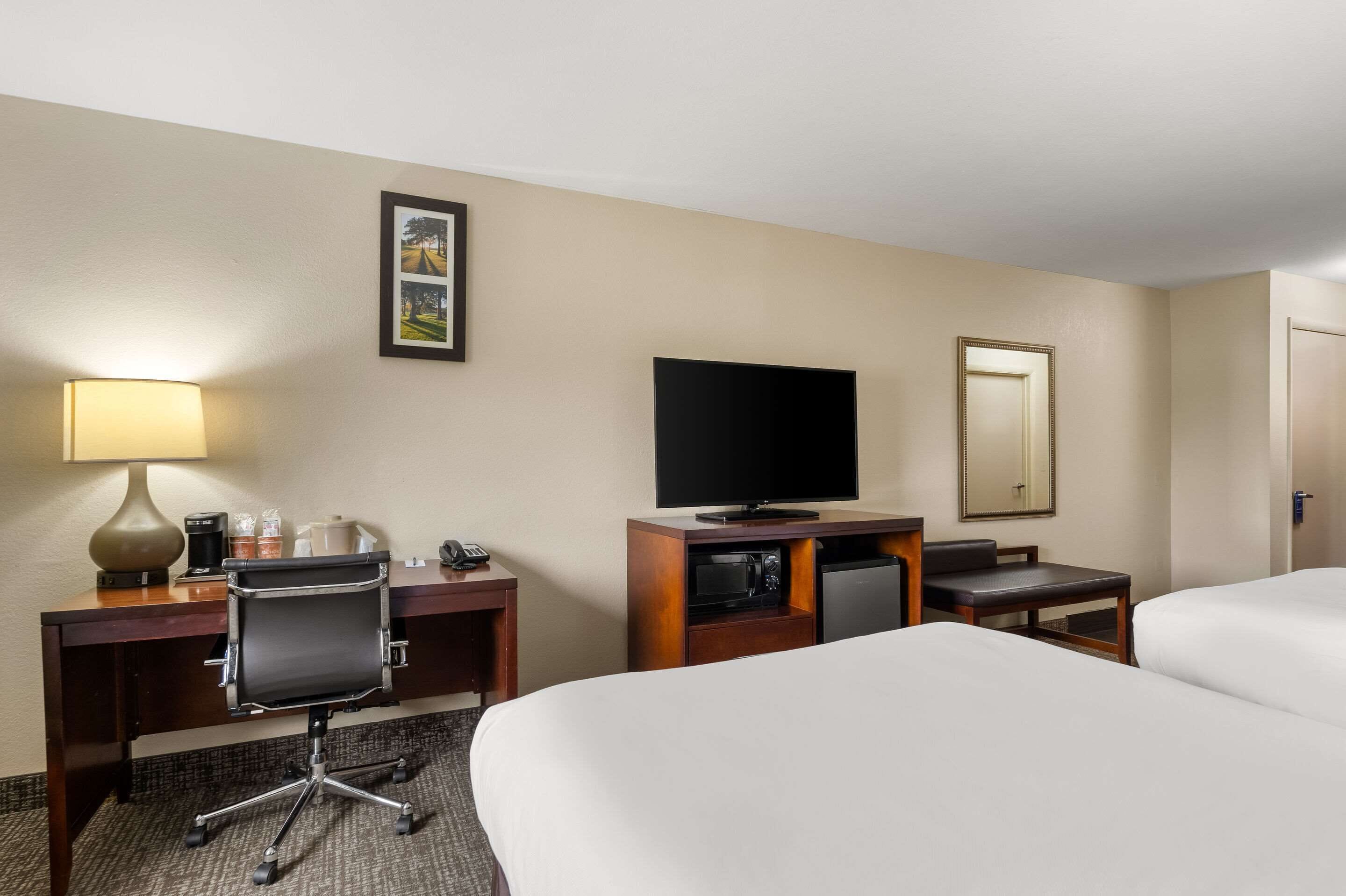A hotel room with two beds, a desk with a lamp, a television, a microwave, and a coffee maker.