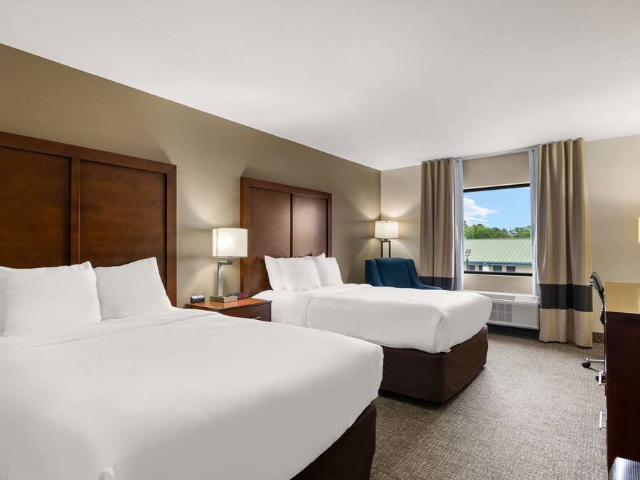 A hotel room with two beds, a desk, a chair, and a window with curtains.