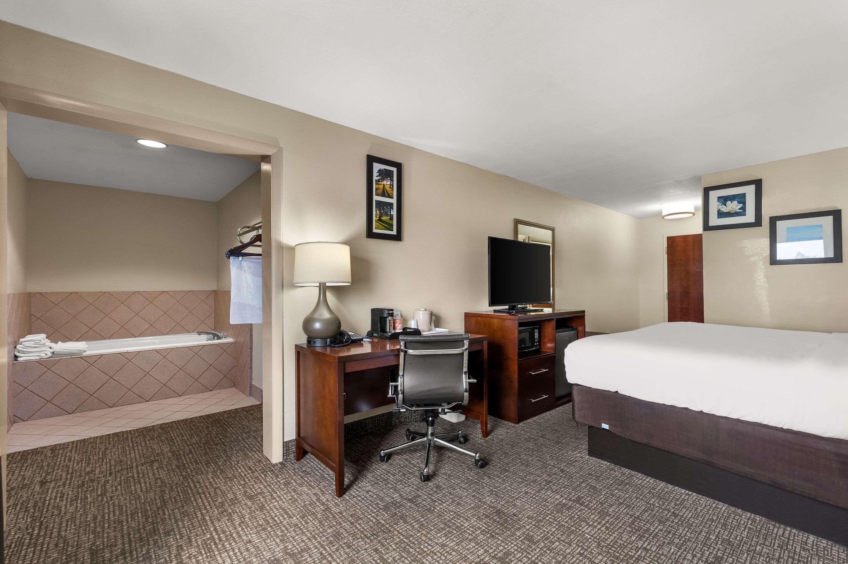 Een hotelkamer met een bed, bureau, stoel, lamp, televisie en een badkamer met een bad en handdoekhouder.