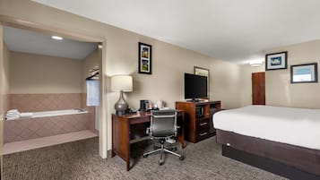 Een hotelkamer met een bed, bureau, stoel, lamp, televisie en een badkamer met een bad en handdoekhouder.
