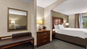 A hotel room with a large bed, a wooden nightstand, a desk with a lamp, a bench, and a large mirror. - Comfort Inn & Suites Chipley (Chipley)