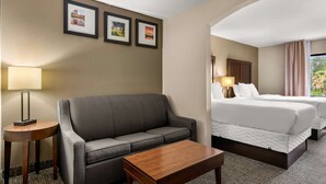 A hotel room with a sofa, a wooden coffee table, a bed with two pillows, and framed pictures on the wall. - Comfort Inn & Suites Chipley (Chipley)