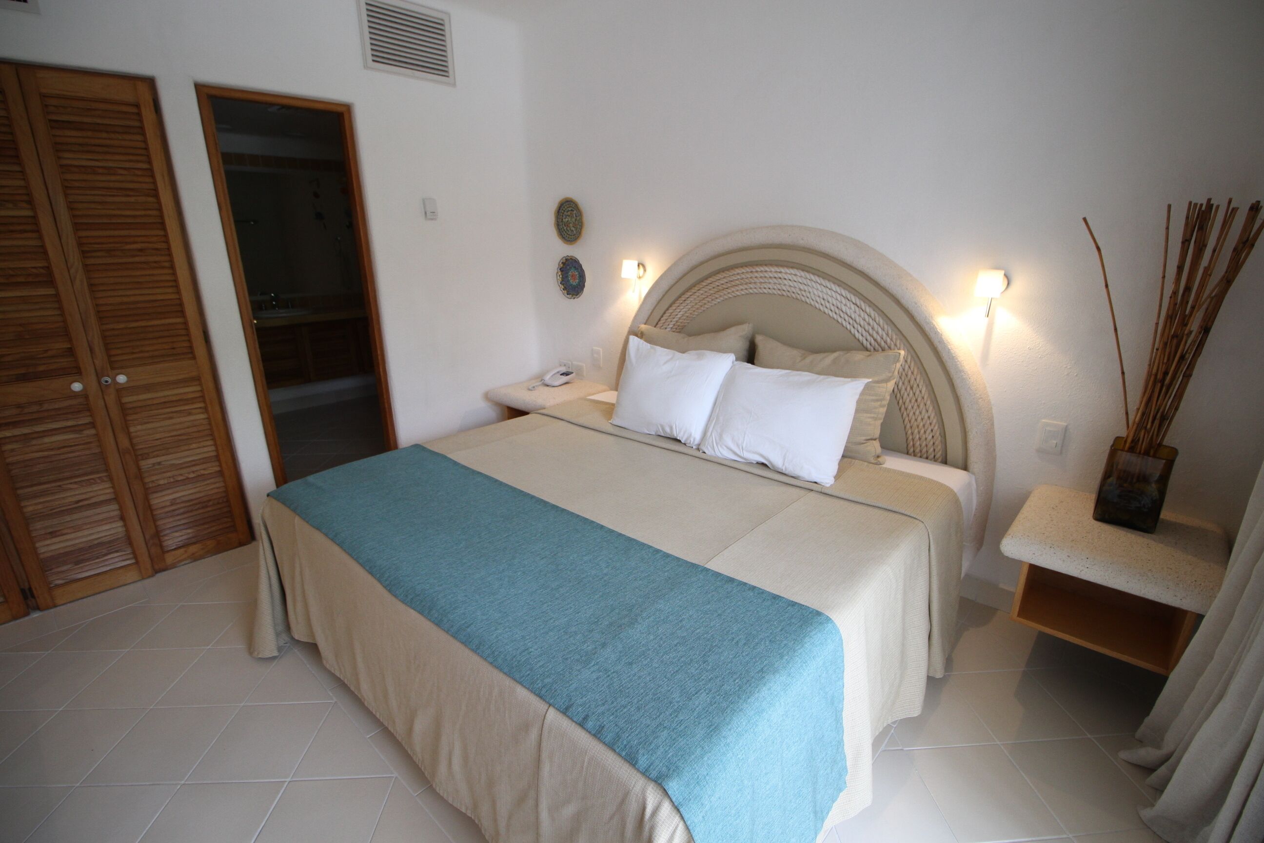 A bedroom with a bed, bedside table, lamp, and a small shelf with decorative items.