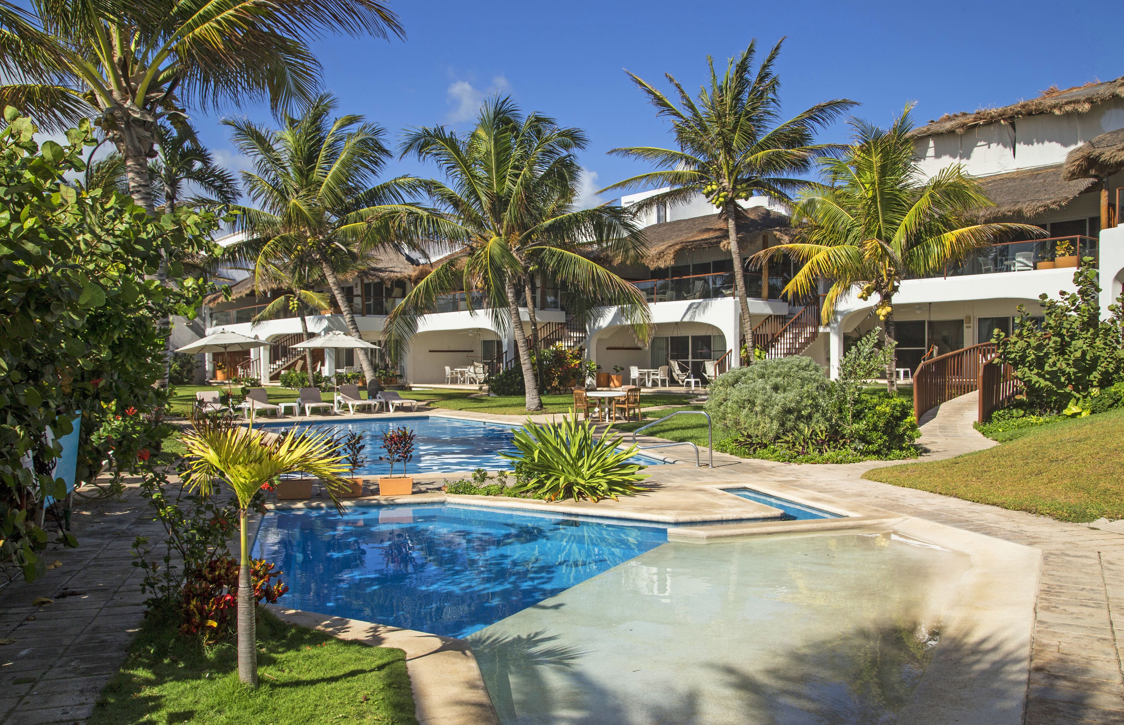 Un resort con varias piscinas, palmeras y un jardín bien cuidado.