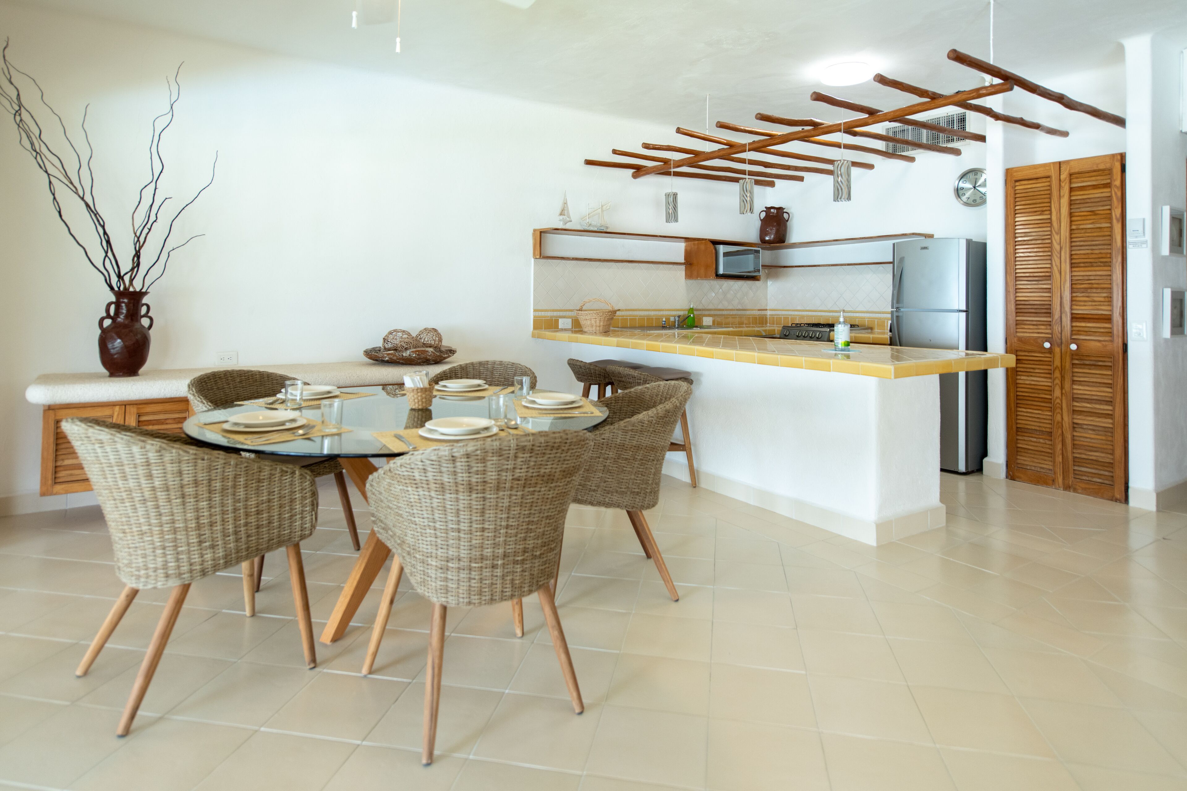 A modern kitchen with a central island, wicker chairs, and a dining table set for four.