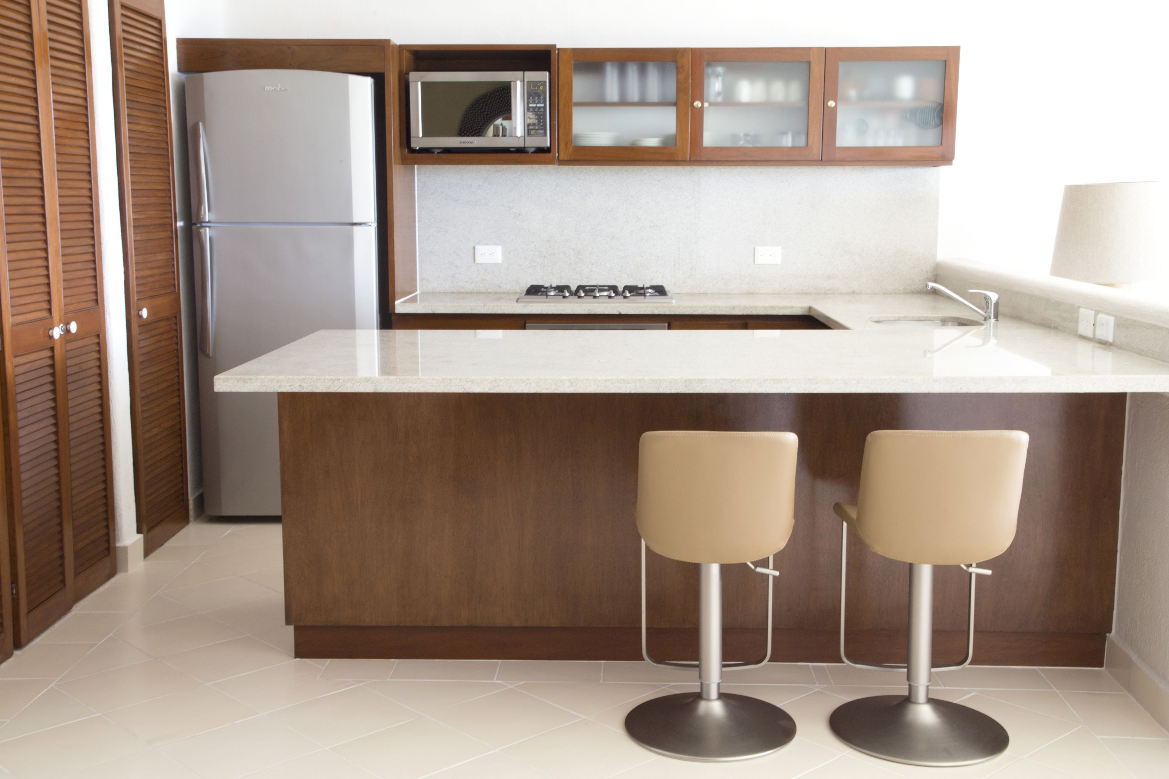 A modern kitchen with a built-in microwave, a stainless steel refrigerator, a gas stove, and two bar stools.