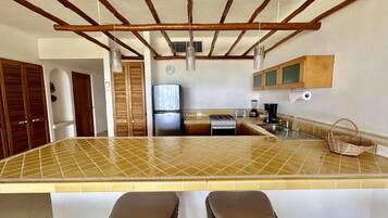 Une cuisine avec un îlot central recouvert de carreaux, des poutres en bois au plafond, un réfrigérateur, une cuisinière et un évier.