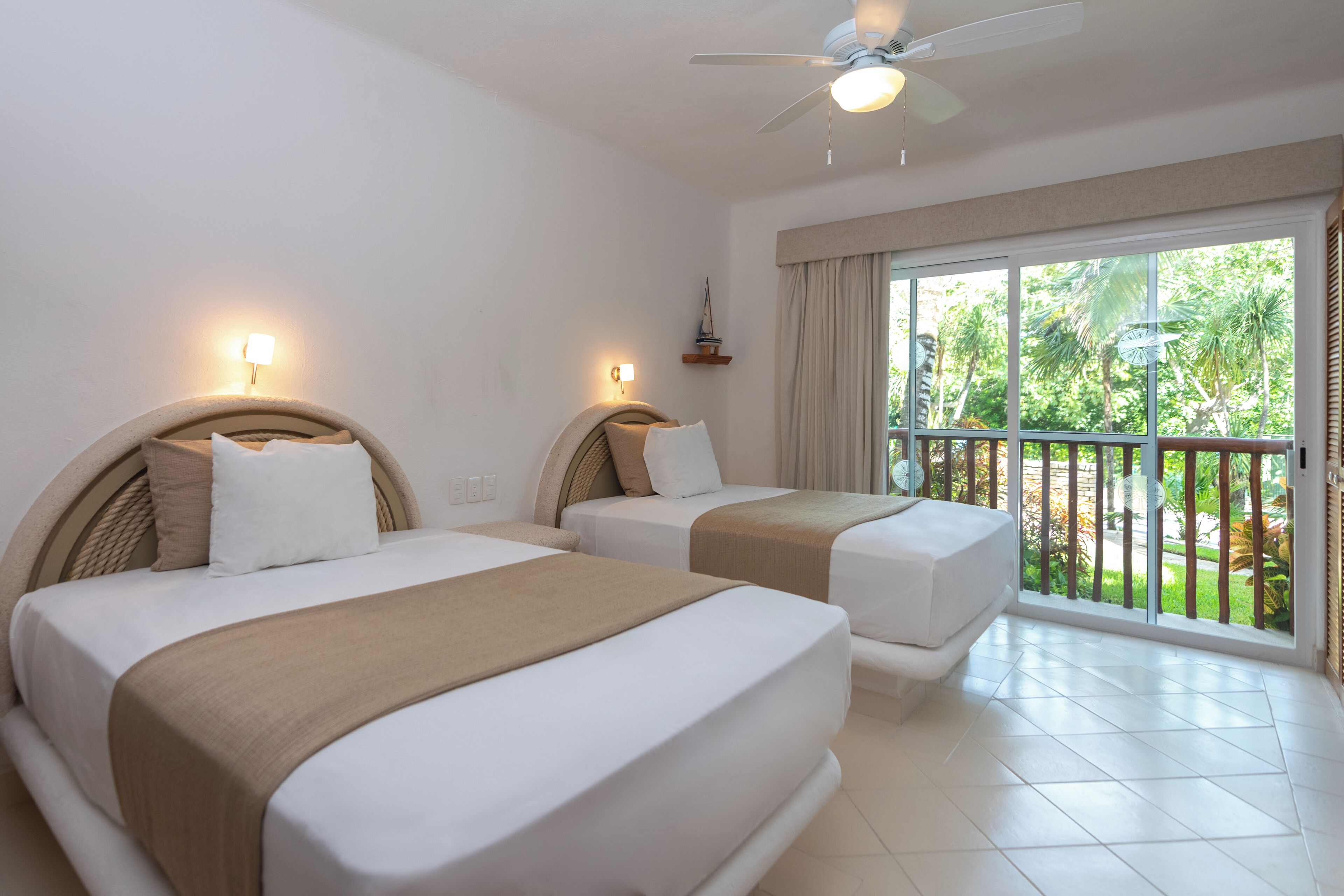 Une chambre d’hôtel avec deux lits, un ventilateur de plafond et un balcon donnant sur un paysage verdoyant.
