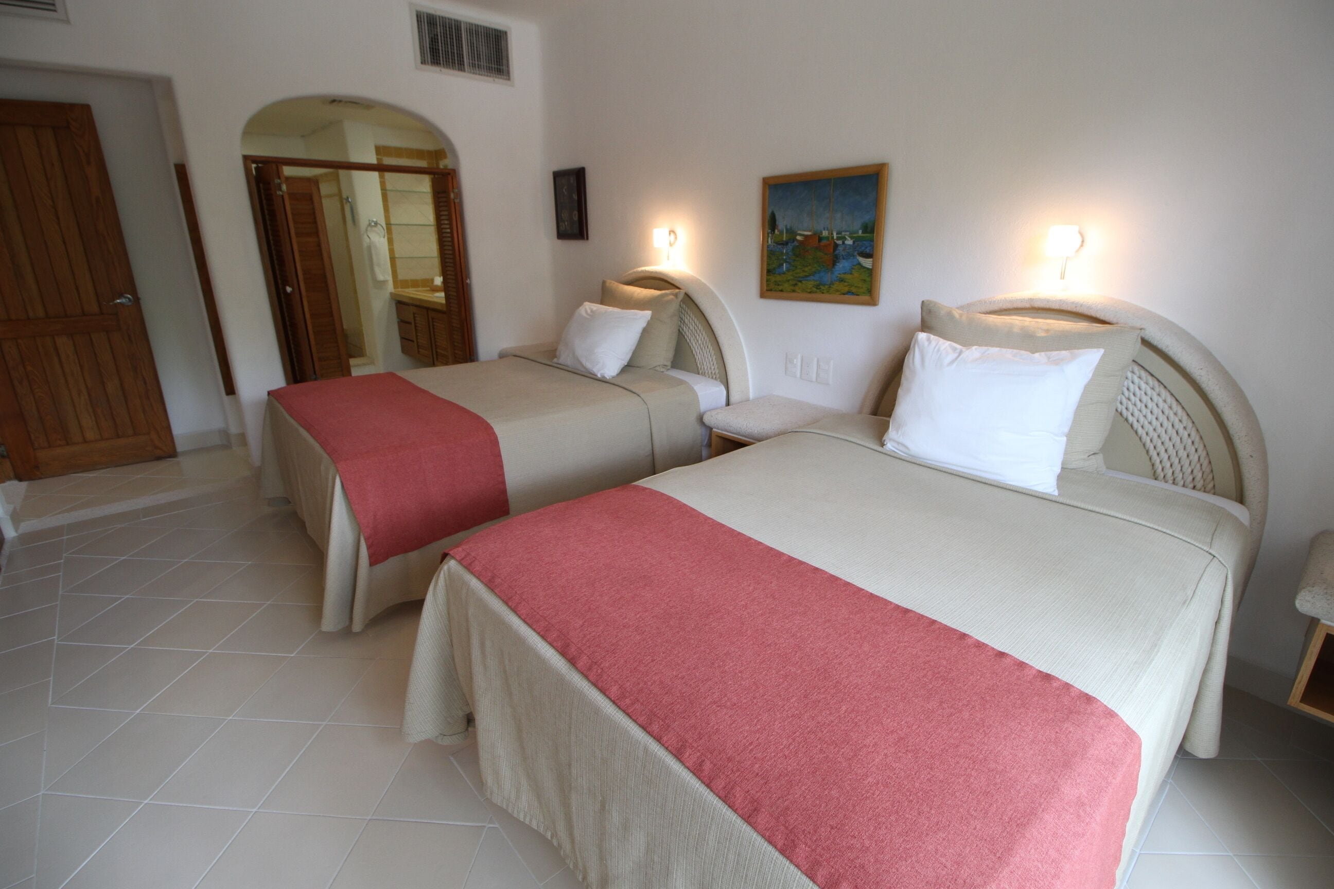 A hotel room with two beds, a bathroom, and a painting on the wall.