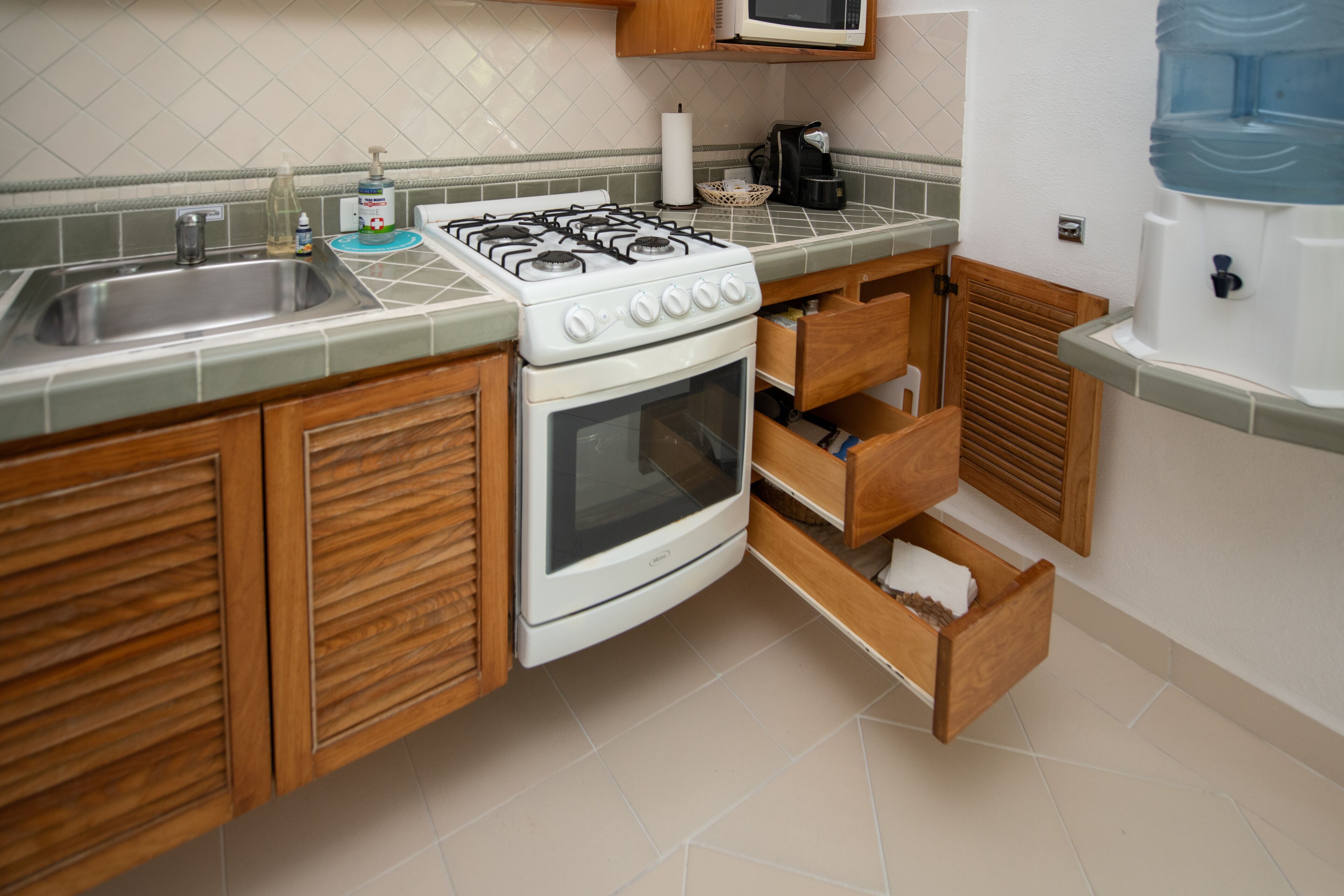 A kitchen with a stove, sink, wooden cabinets, and a water dispenser.