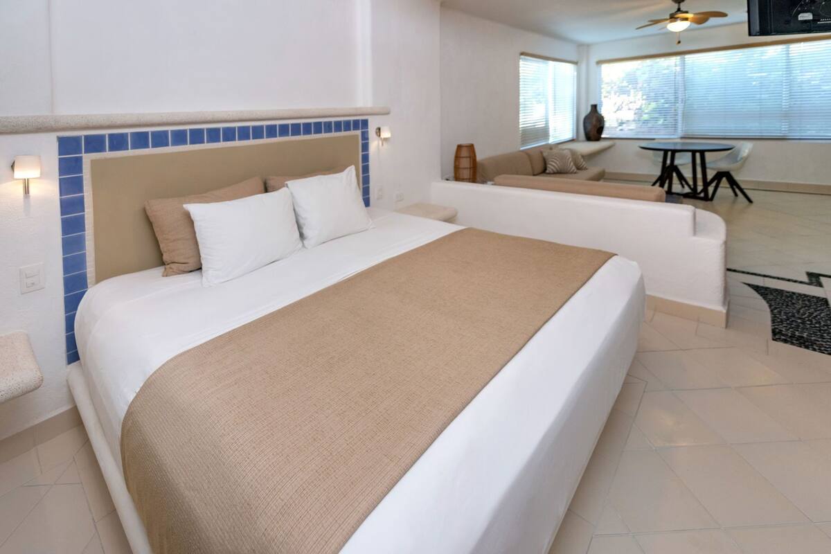 A hotel room with a large bed, a sofa, a small table, and a ceiling fan.
