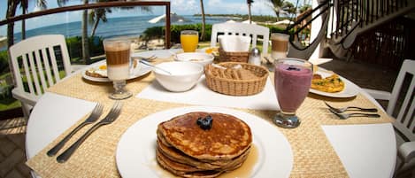 Et morgenbord med pandekager, et glas appelsinjuice og udsigt til havet.