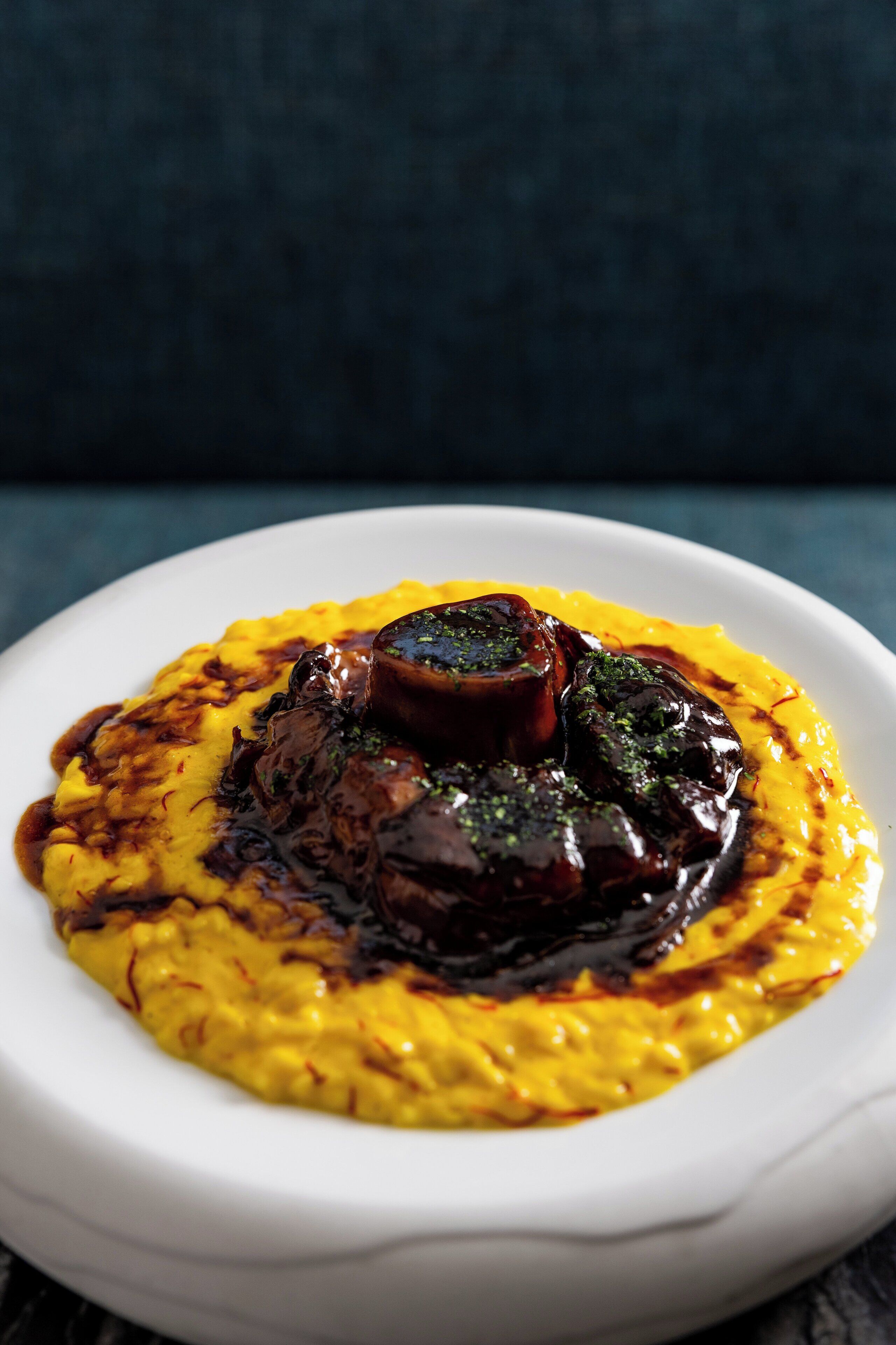 Ein weißer Teller mit gelbem Polenta und einer dunklen Soße, vermutlich Pilsoße, vor dunklem Hintergrund.