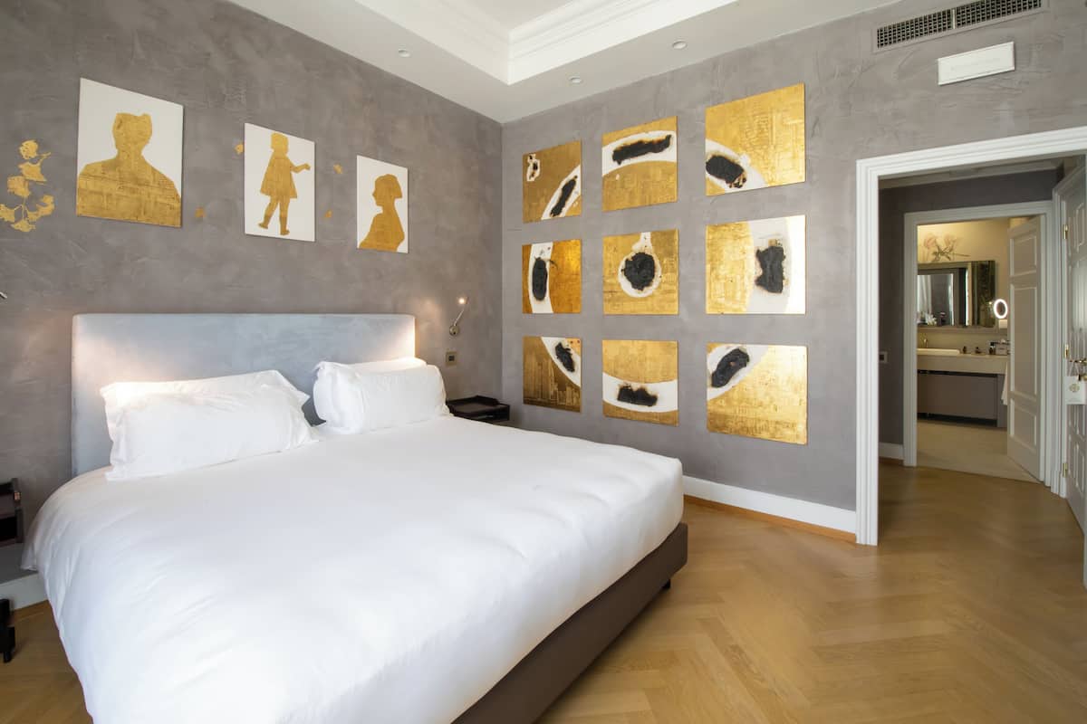 Une chambre moderne avec un grand lit, une table de chevet et un mur orné de plusieurs œuvres d’art encadrées.