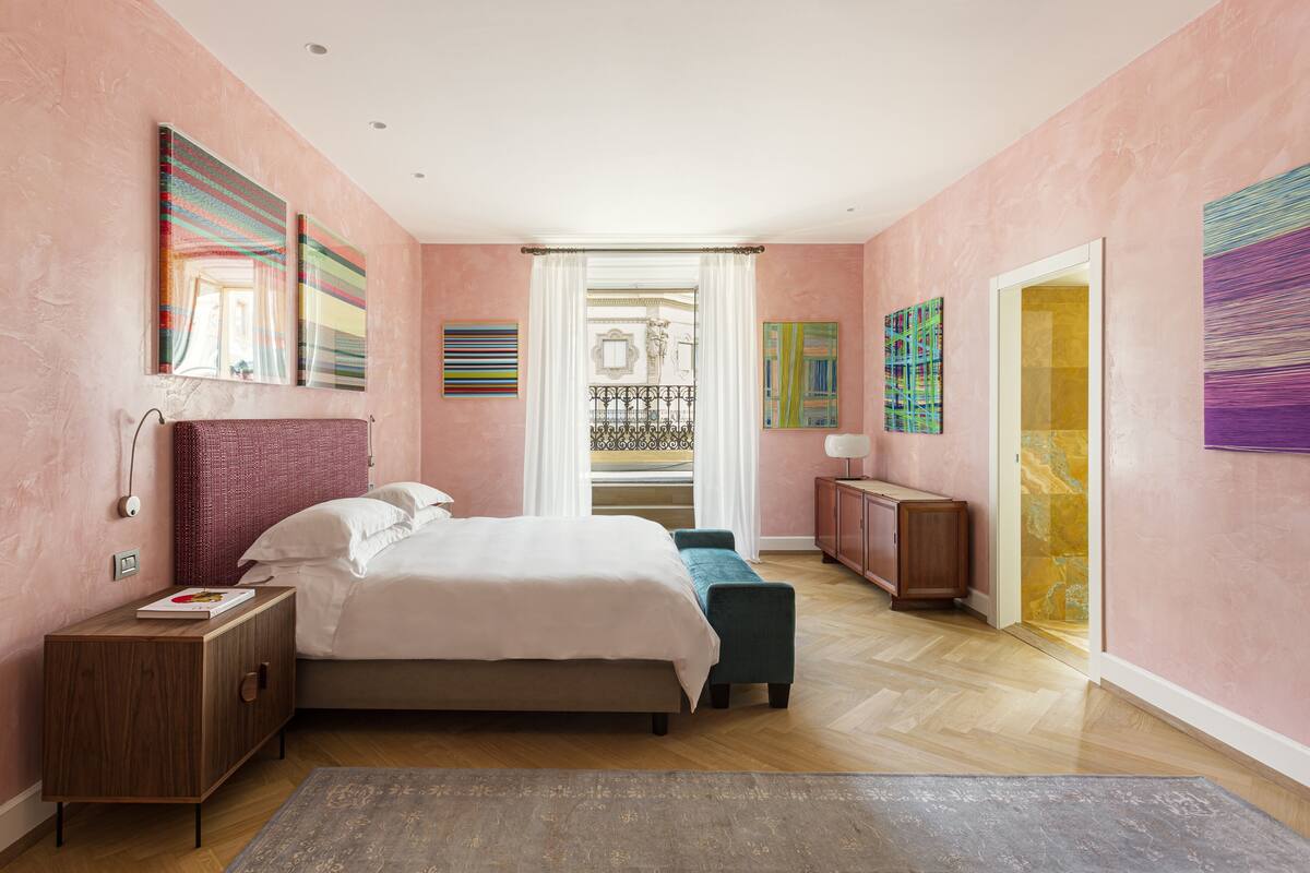 Une chambre à coucher avec un lit, des tables de chevet, un banc et des œuvres d’art accrochées aux murs.