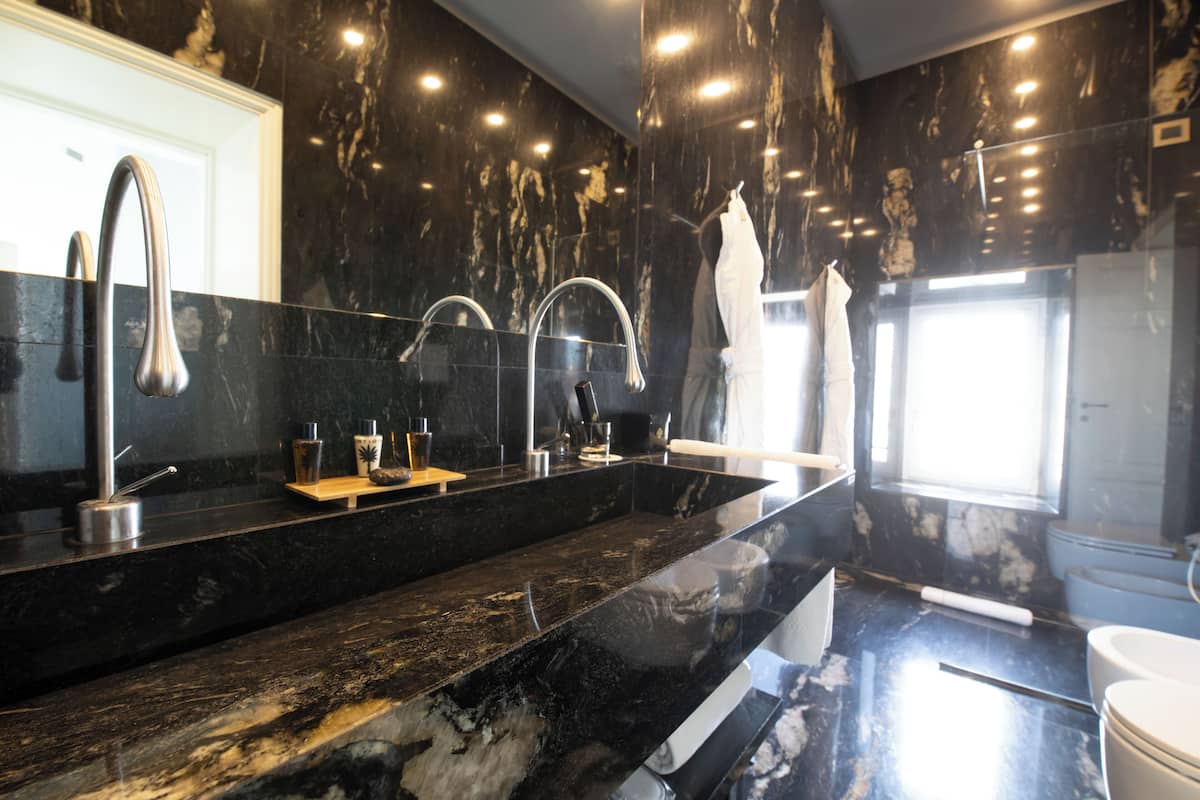 Une salle de bain moderne avec un comptoir en marbre noir, deux vasques et un grand miroir.