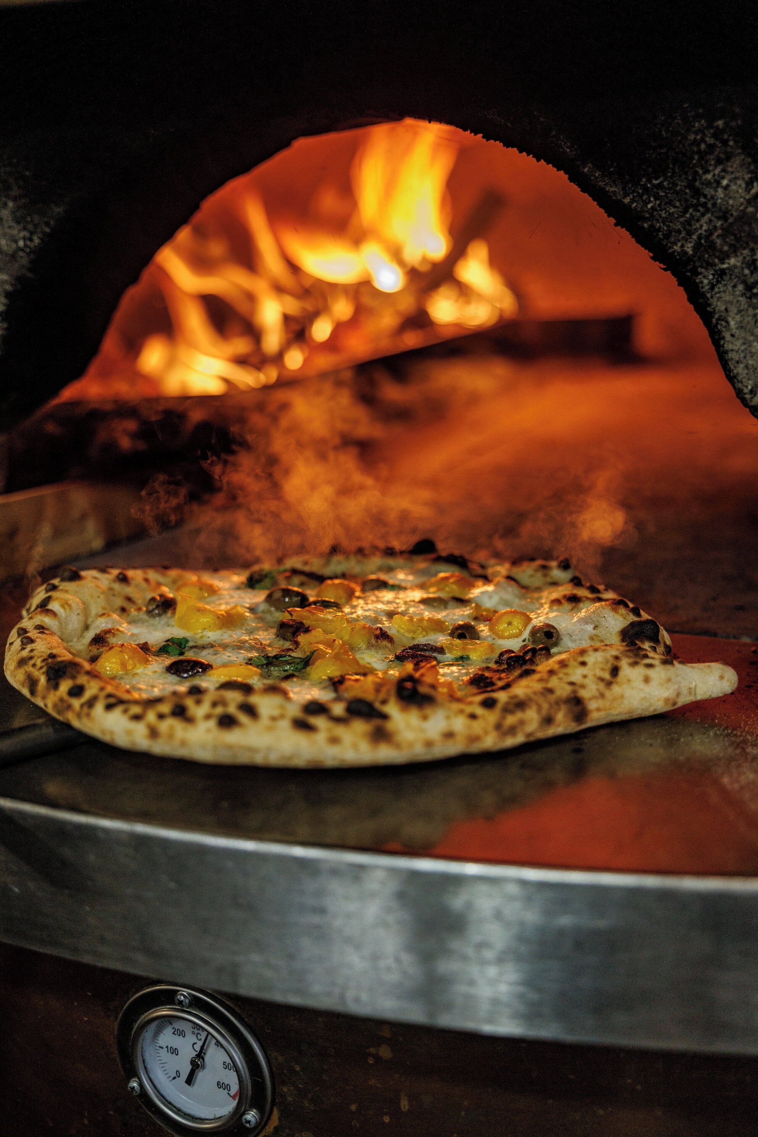 Una pizza en un horno de leña con un termómetro digital debajo.