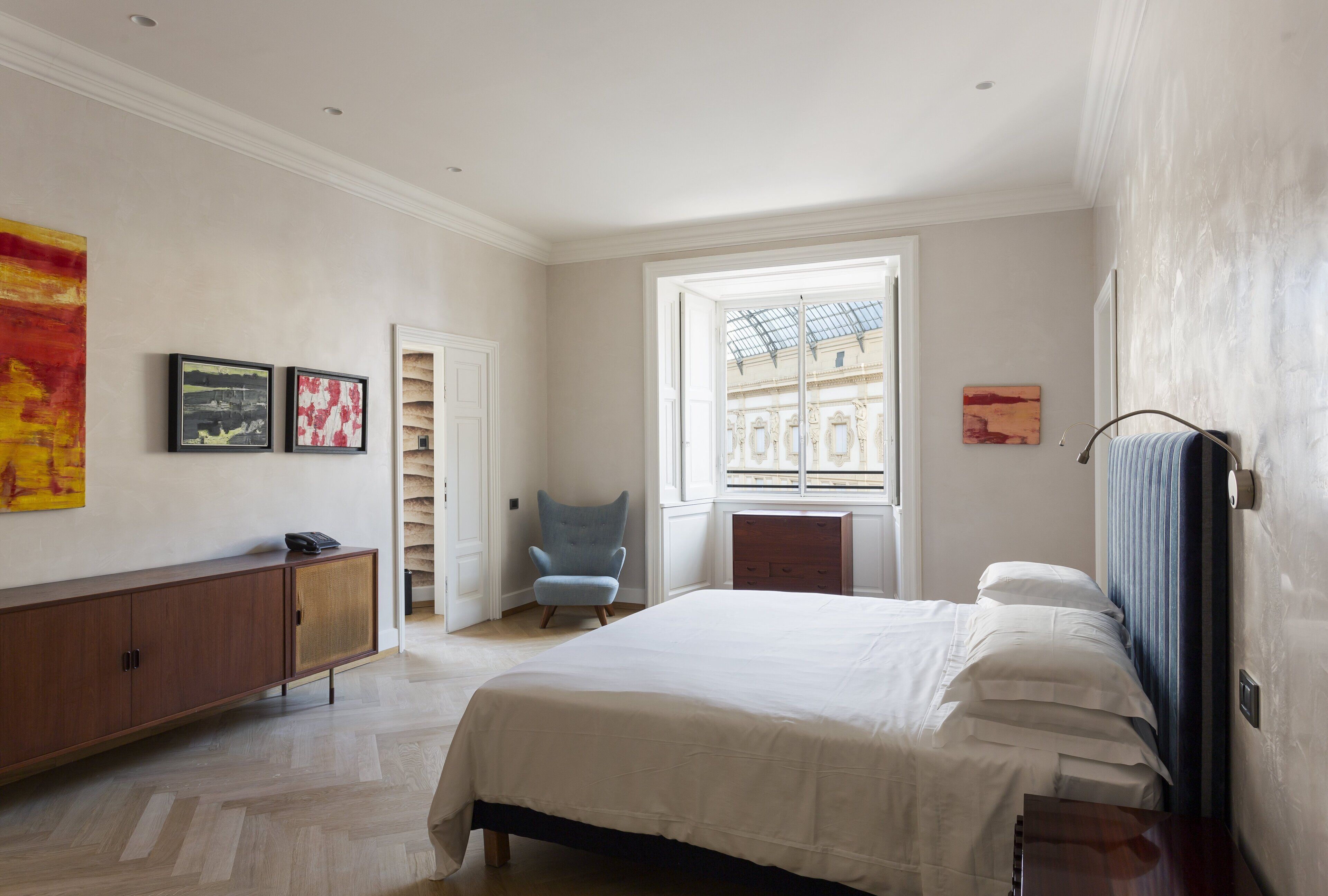 Ein Schlafzimmer mit Bett, Stuhl, Kleiderschrank und Fenster mit Blick auf Gebäude.