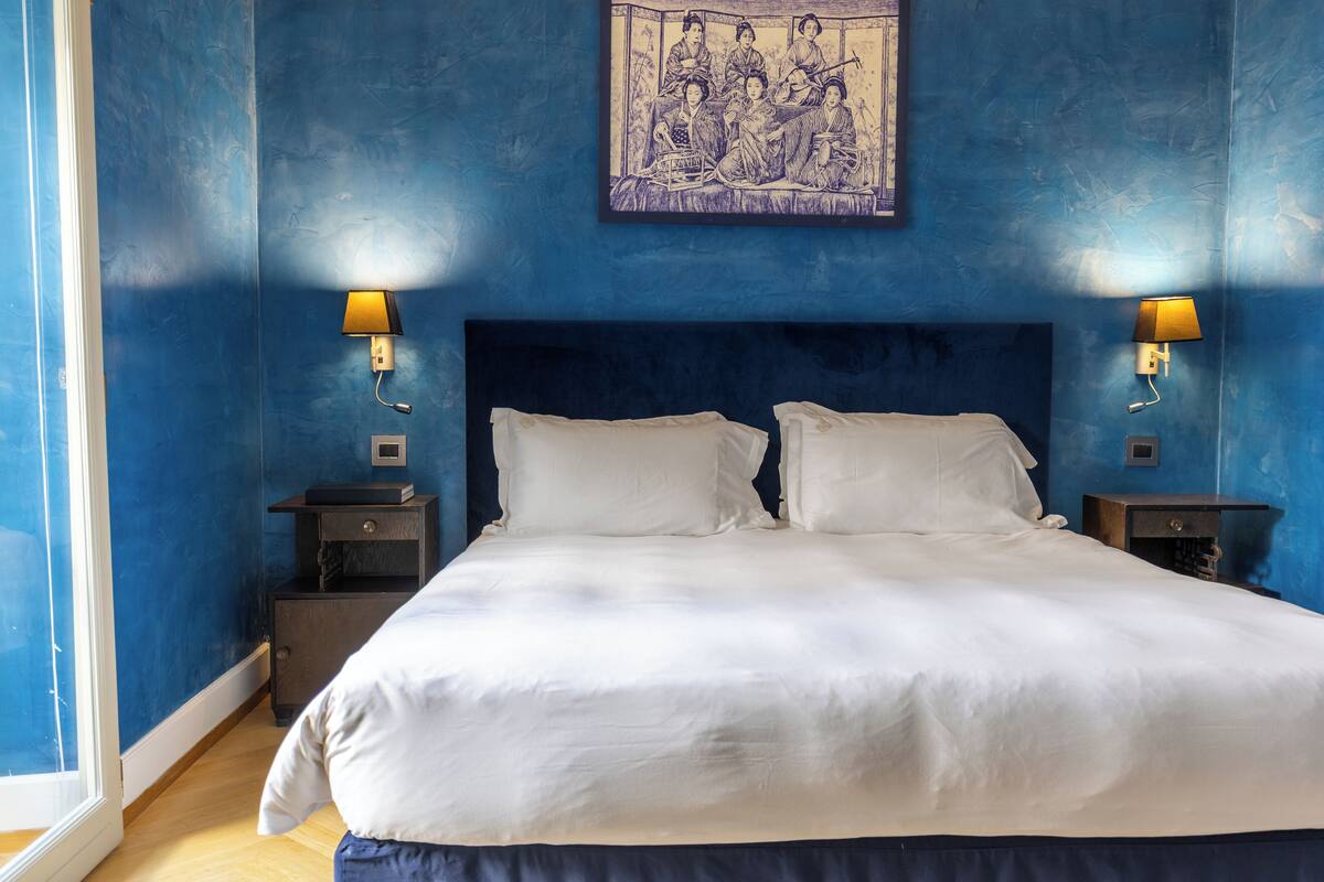Une chambre à coucher avec un grand lit, deux tables de chevet, une tête de lit et une œuvre d’art accrochée au mur.