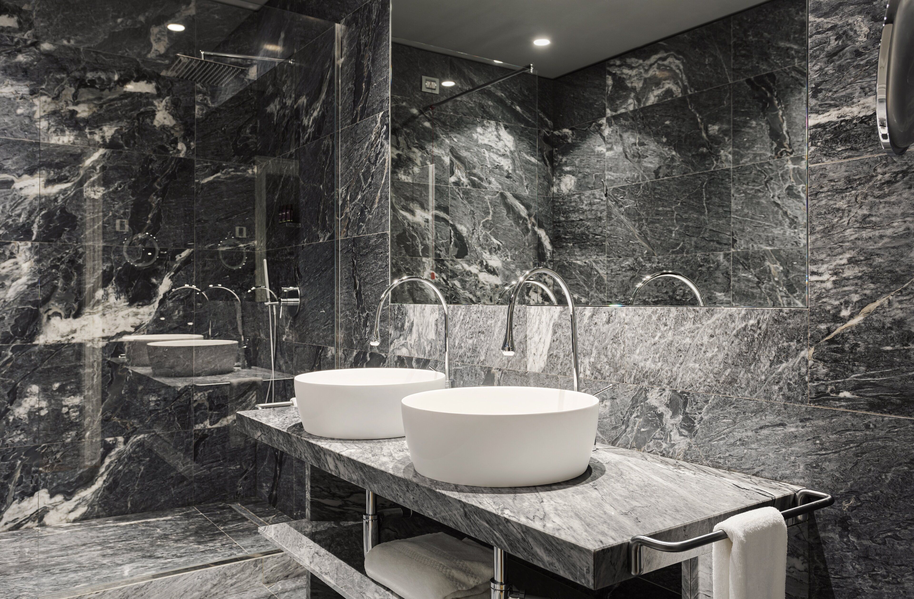 A modern bathroom with two round sinks, a large mirror, and a shower area.