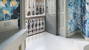 Un baño moderno con vistas a un edificio histórico a través de una puerta de cristal, suelo de mármol y un espejo grande.