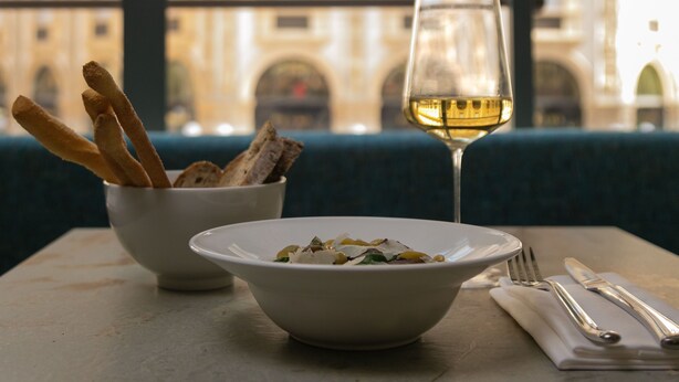 Una mesa de comedor con un tazón de ensalada, una copa de vino blanco y un recipiente con palitos de pan.