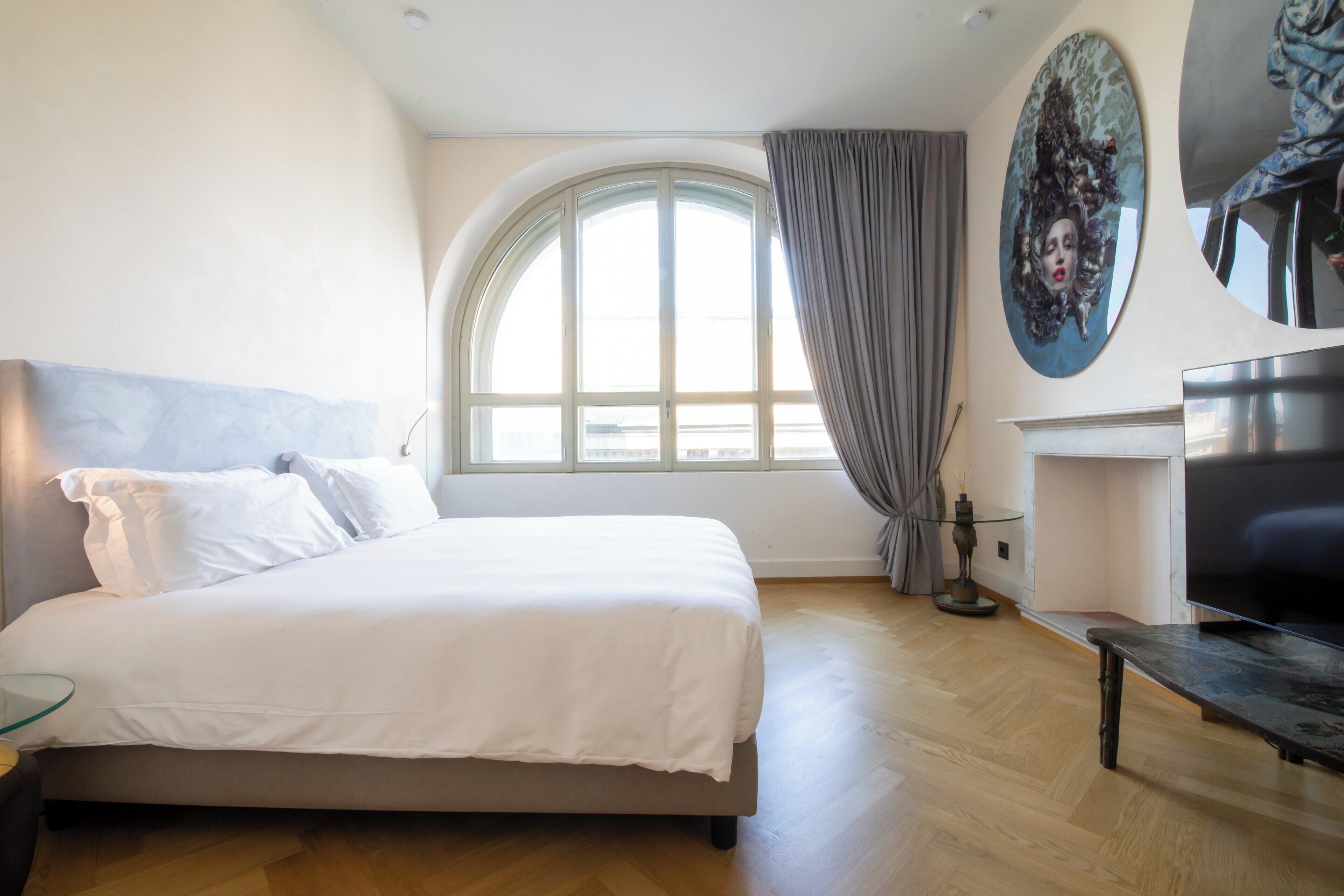 Une chambre à coucher avec un grand lit, une télévision, une cheminée et une grande fenêtre avec des rideaux.