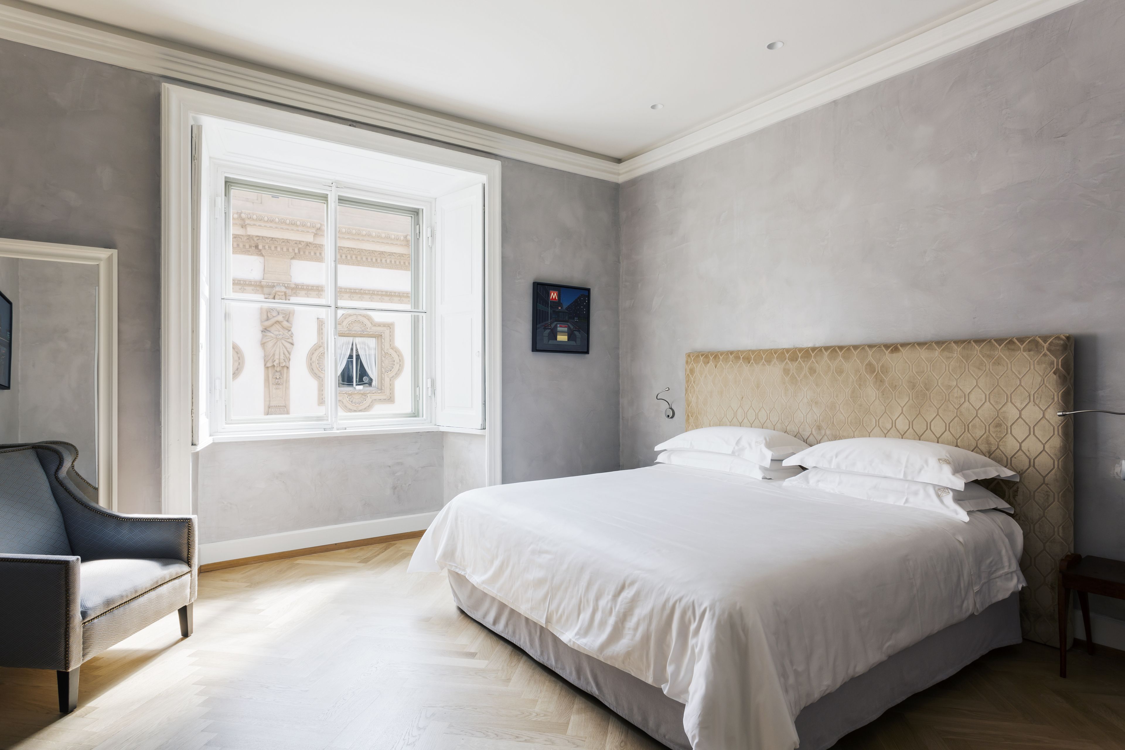 A bedroom with a large bed, a chair, a window, and a framed picture on the wall.