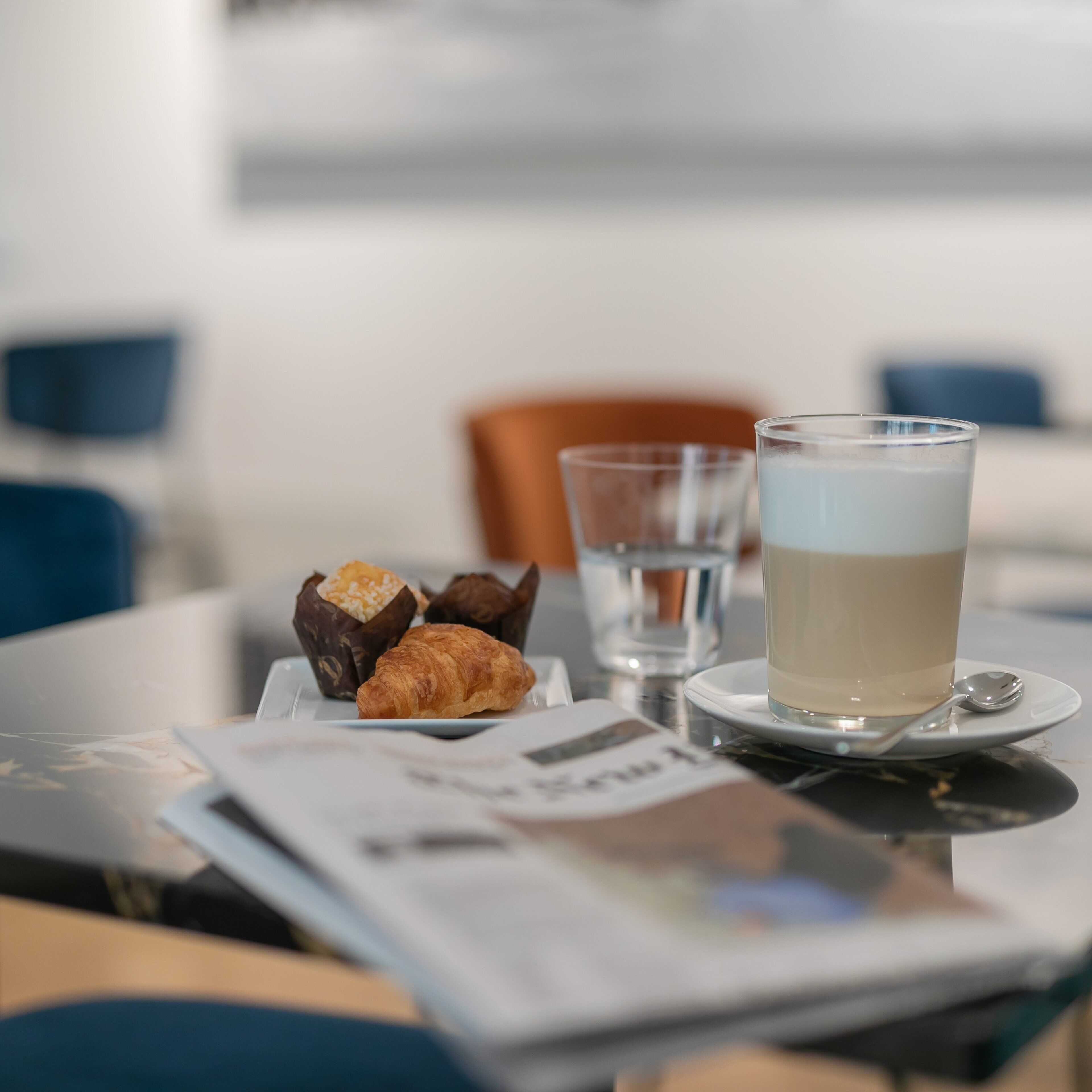 A table with a croissant, a glass of coffee, and a glass of water.