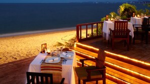 Un área de comedor frente a la playa con mesas dispuestas para dos, con vista al océano.