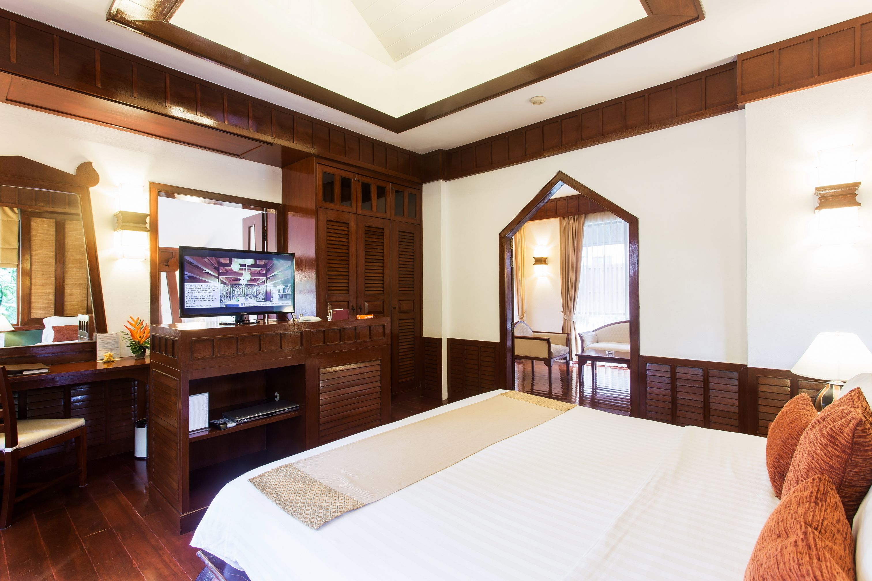 A hotel room with a large bed, a desk with a television, a mirror, and a wooden wardrobe.