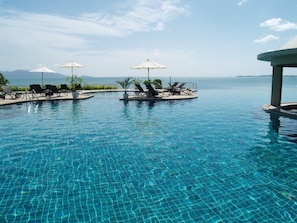 Una piscina al aire libre, sombrillas, sillones reclinables de piscina