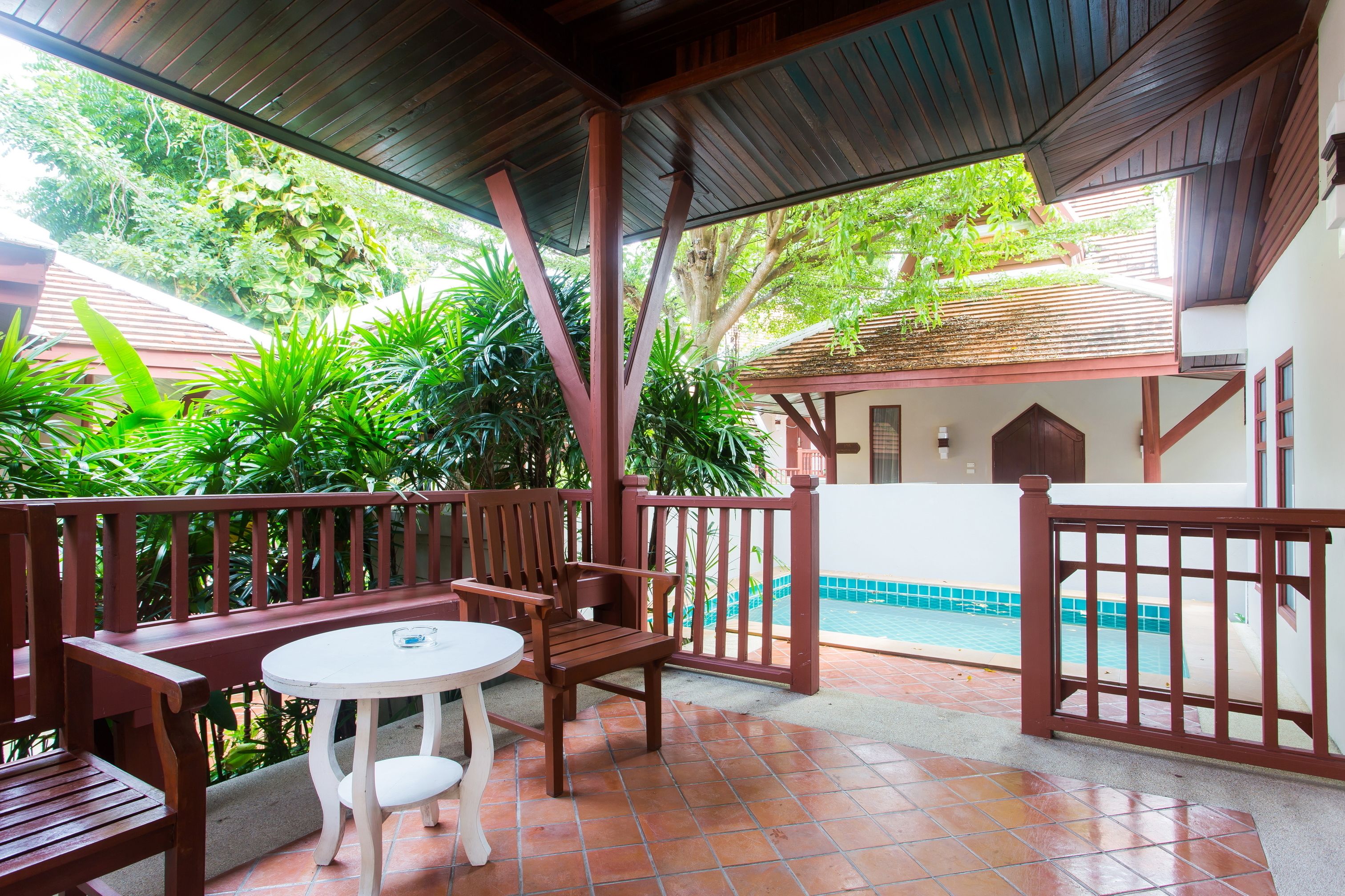 Un patio techado con mobiliario de madera, piso de baldosas y vista a una piscina.