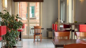 Un restaurante con una decoración moderna, que presenta muebles rojos y de madera, una planta grande en maceta y vistas de la ciudad a través de las ventanas.