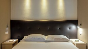 Una habitación de hotel con una cama grande, dos mesitas de noche y un cabecero oscuro.